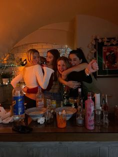 three girls are hugging in front of a counter full of liquor bottles and other items