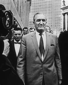 a man in a suit and tie walking down the street with other men behind him