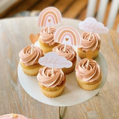 cupcakes with pink frosting on a white plate and wooden chairs in the background