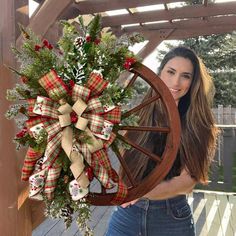 a beautiful woman holding a christmas wreath on top of a wagon wheel