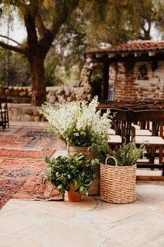 two baskets filled with flowers sitting on top of a stone floor next to chairs and tables