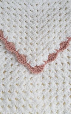 a crocheted blanket is laying on top of a white tablecloth with pink trim