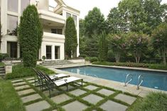 an empty swimming pool in front of a large house with lawn and steps leading up to it