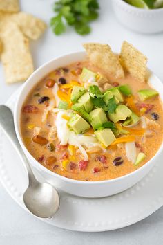 a white bowl filled with soup and topped with avocado, sour cream and tortilla chips