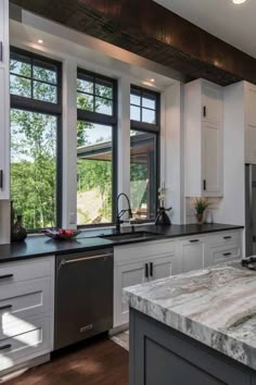 a kitchen with marble counter tops and stainless steel appliances, along with large windows that look out onto the trees