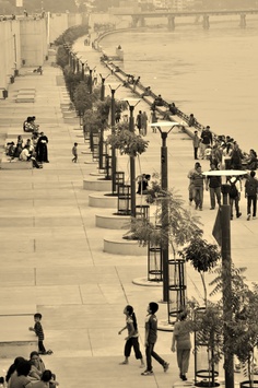 black and white photograph of people walking on sidewalk next to water