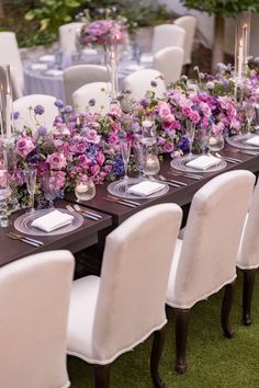 a long table with white chairs and purple flowers