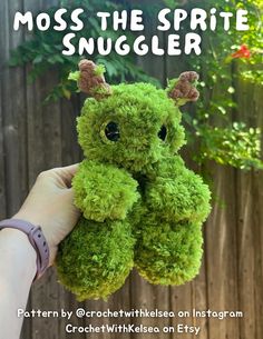 a hand holding a green stuffed animal with the words moss the spirit snuggler