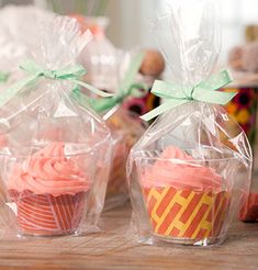 three cupcakes wrapped in plastic and sitting on a table next to some candy