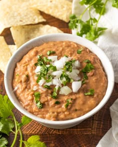 a white bowl filled with guacamole surrounded by tortilla chips and cilantro