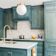 a kitchen with blue cabinets and white counter tops, gold faucet lighting over the sink