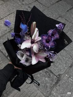 a person holding a bouquet of flowers on top of a black cloth covered hat with purple and white flowers