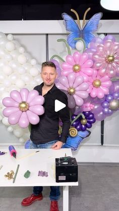 a man standing in front of a table with balloons and flowers on the wall behind him