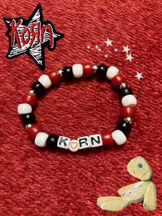 a red and white beaded bracelet with the word kron on it next to a small teddy bear