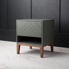 a small grey cabinet with wooden legs on a white tile floor in front of a black wall