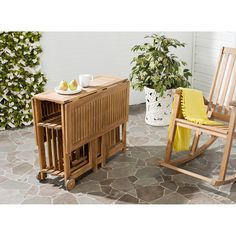 a wooden rocking chair next to a table with fruit on it and a potted plant