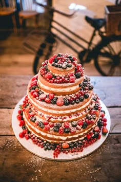 a wedding cake with berries and powdered sugar on top sits on a wooden table