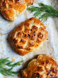 three pastries sitting on top of a piece of parchment paper next to green sprigs