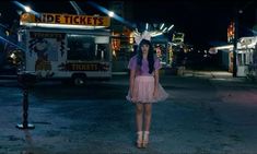 a woman standing in the middle of an empty parking lot at night with food trucks behind her