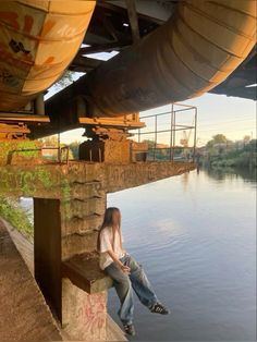 a woman sitting on the edge of a bridge next to a body of water with graffiti