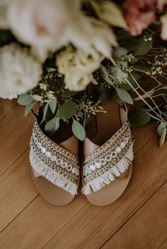 the bride's shoes are adorned with beading and flower petals, along with greenery