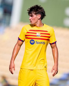 a soccer player in yellow and red uniform on the field with his head turned to the side