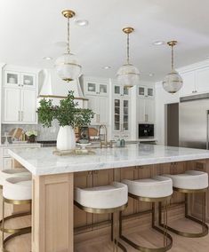 a large kitchen with white cabinets and marble counter tops, gold accents and stools