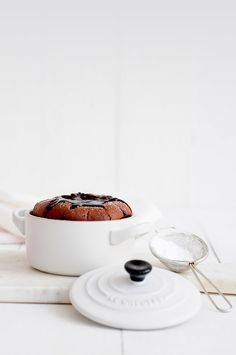 a chocolate cake in a white casserole on a table with a spatula next to it