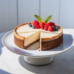 a cheesecake with berries on top sits on a white cake plate and is ready to be eaten