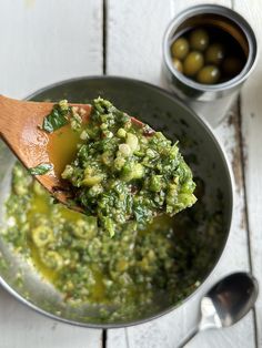 a wooden spoon full of pesto sauce on top of a white table next to some olives