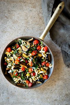 a bowl filled with pasta and vegetables on top of a table next to a wooden spoon