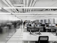 an office with desks, computers and people in the distance walking through the room