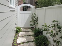 a white gate and walkway leading to a house with green plants on the side walk