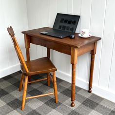 a laptop computer sitting on top of a wooden desk next to a chair and coffee cup