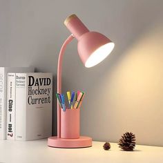 a pink desk lamp sitting on top of a table next to a stack of books