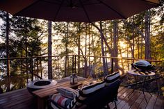 a deck with two chairs and an umbrella over it that is overlooking the water at sunset