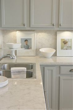 a white kitchen with marble counter tops and stainless steel sink in front of a framed photograph