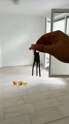 a hand holding two keys in the middle of a room with white tile flooring