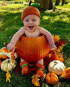 a baby in a pumpkin costume sitting on the grass