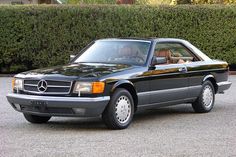 a black mercedes benz parked in front of a hedge