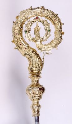 an ornate gold and silver object on a white surface with a small figure in the center