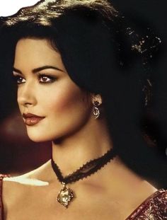 a woman with dark hair wearing a necklace and earrings