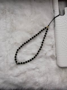 a black beaded necklace with a white leather case on a fur rug next to it