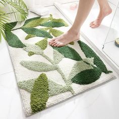 a person standing on a bathroom rug with green leaves in the middle and white floor