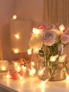 a vase filled with pink roses sitting on top of a table next to some lights