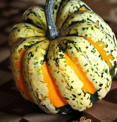 a close up of a small pumpkin on a checkered table cloth with an orange and black stripe