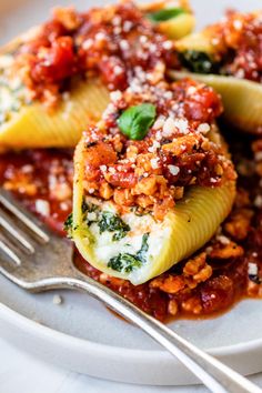 a white plate topped with stuffed shells covered in sauce and cheese next to a fork