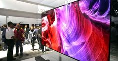 people are standing around looking at the large television screen in the store's display area