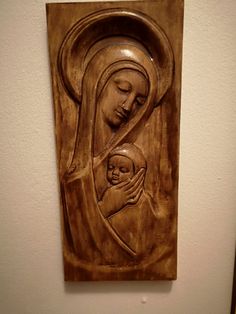 a wooden carving of the virgin mary holding a baby jesus in her arms on a white wall