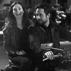 a man and woman riding on the back of a motorcycle